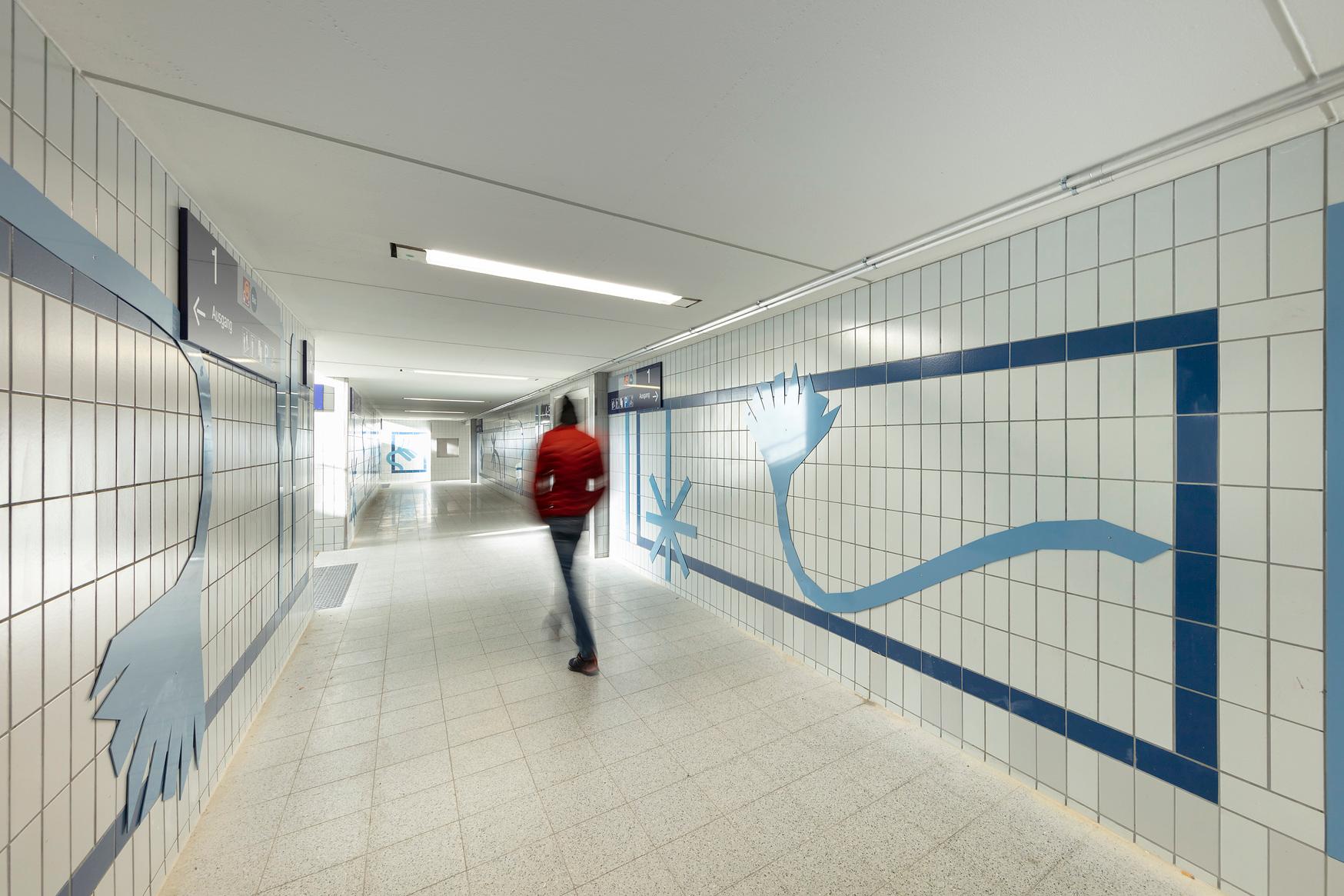 Personenunterführung mit weißen Fliesen und blauen Designelementen.